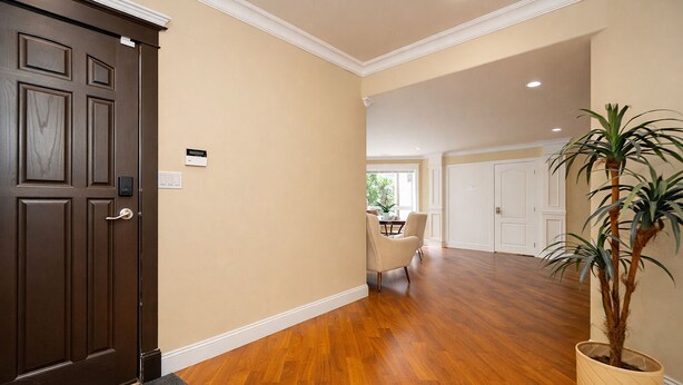 A hallway with wooden flooring, beige walls, a dark brown door, and a potted plant.