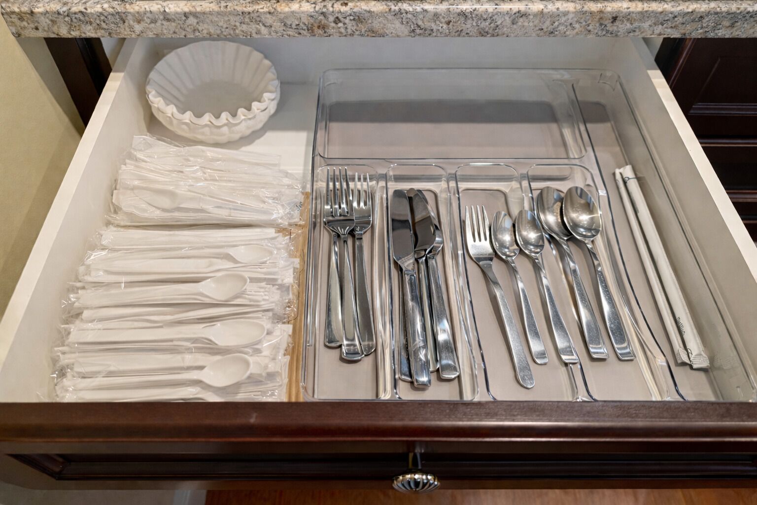 A drawer containing neatly arranged silverware, plastic spoons, and a white paper plate.