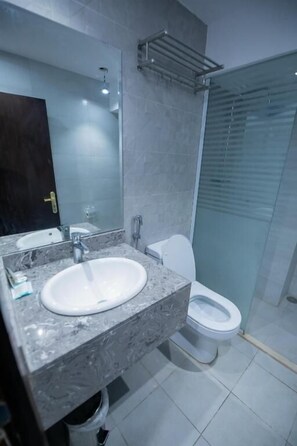 A modern bathroom with a marble sink, a glass shower enclosure, and a white toilet.