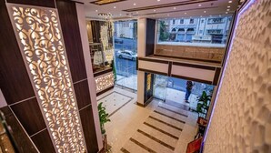 En moderne hotellobby med en dekorativ væg, en lysekrone og udsigt til gaden.