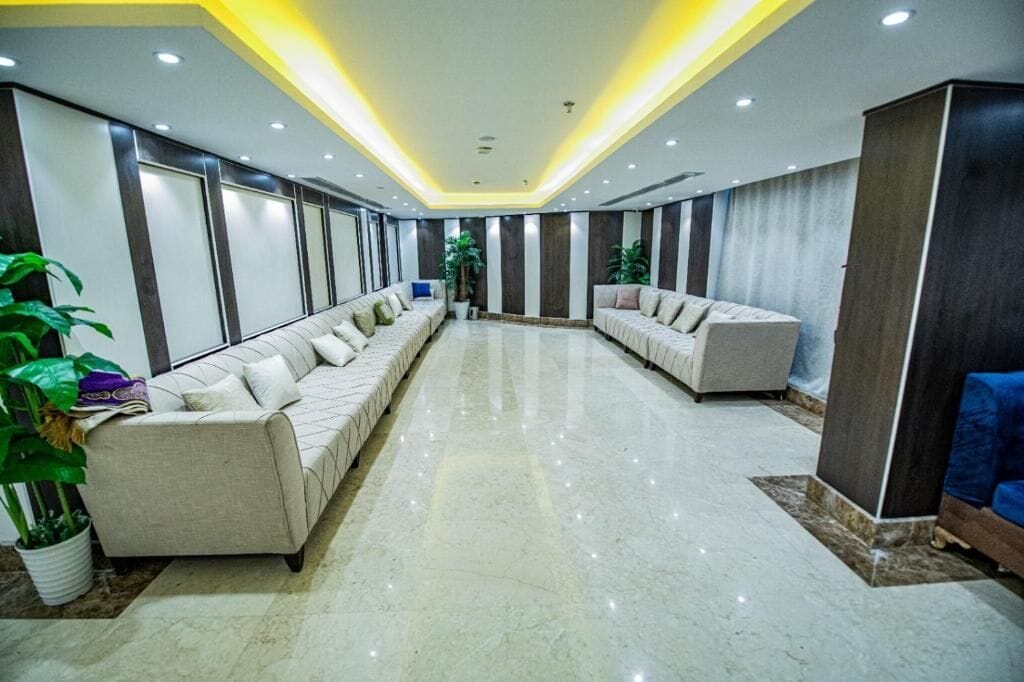 A spacious hotel lobby with a long reception area, two sofas, and a large potted plant.