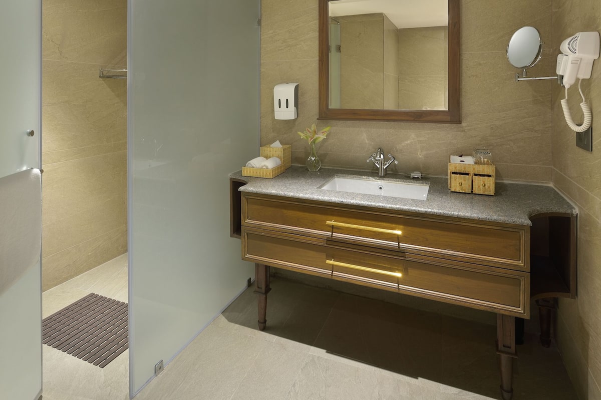 A modern bathroom with a glass shower enclosure, a vanity with a sink, a mirror, and a hairdryer mounted on the wall.