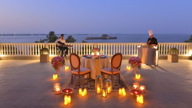 A romantic outdoor dining setup with a table and chairs, candles, and a view of the sea. - The Fort House, Diu- IHCL SeleQtions (Diu)