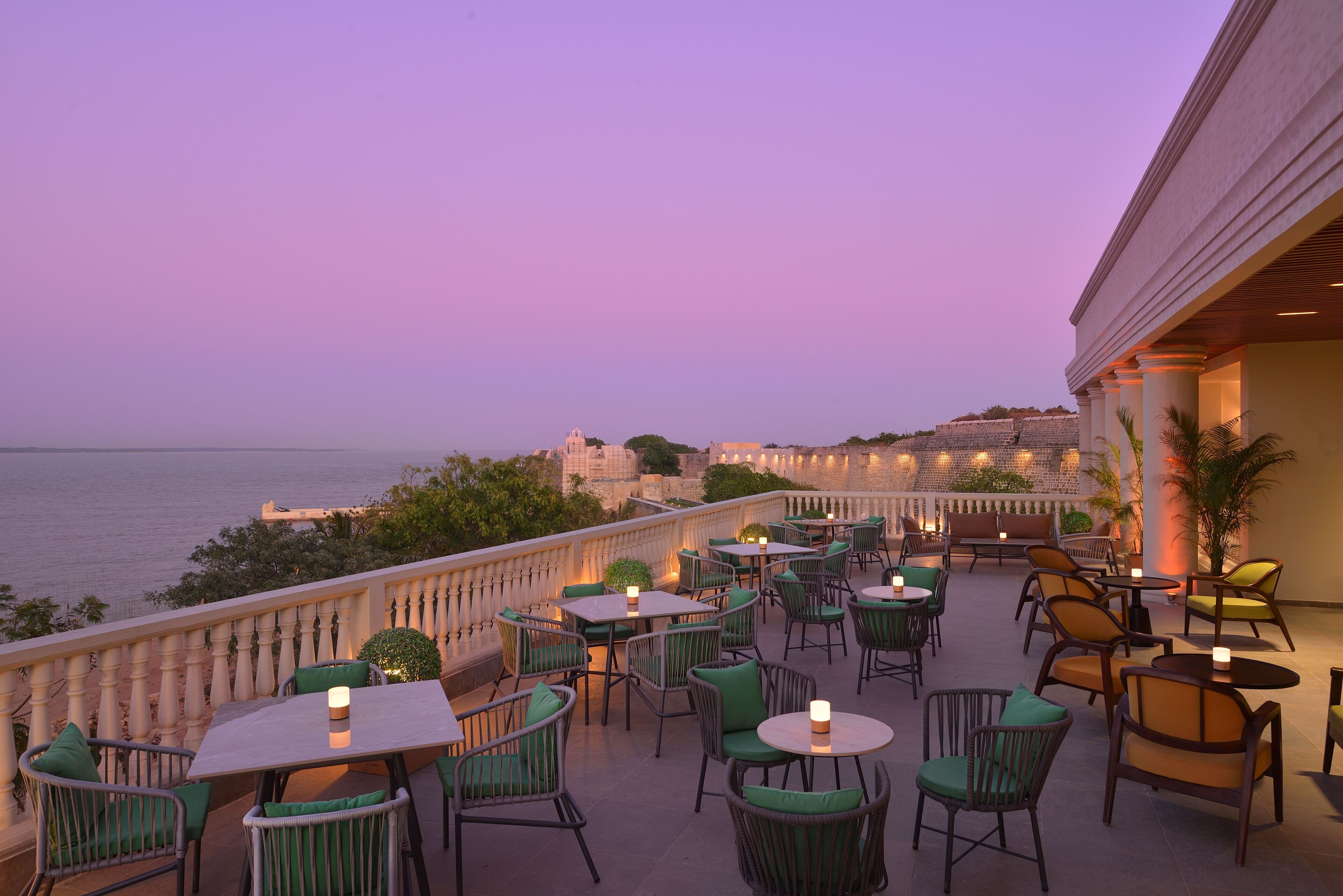 Une terrasse extérieure avec des tables et des chaises, offrant une vue sur une étendue d’eau et sur le paysage urbain au loin.