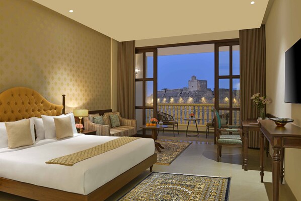 A hotel room with a large bed, a balcony with a view of a historic building, and a dining area with chairs and a table. - The Fort House, Diu- IHCL SeleQtions (Diu)