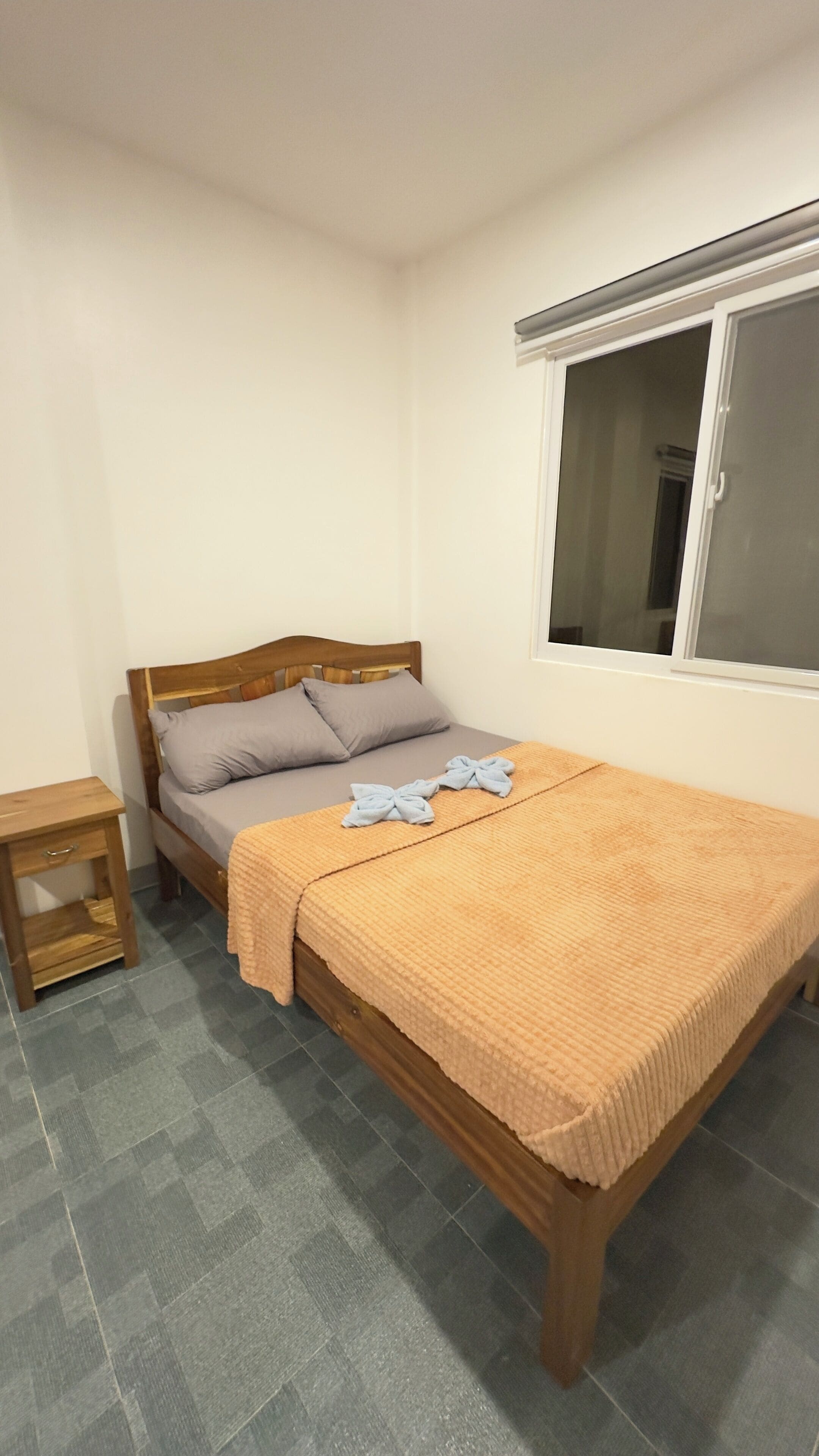 A small, neatly arranged bedroom with a single bed, a bedside table, and a window.