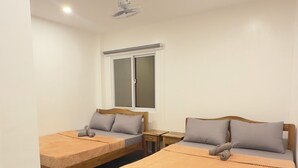 A room with two beds, a wooden table, and a window with frosted glass. - The Palawans Place-b&b (Puerto Princesa)