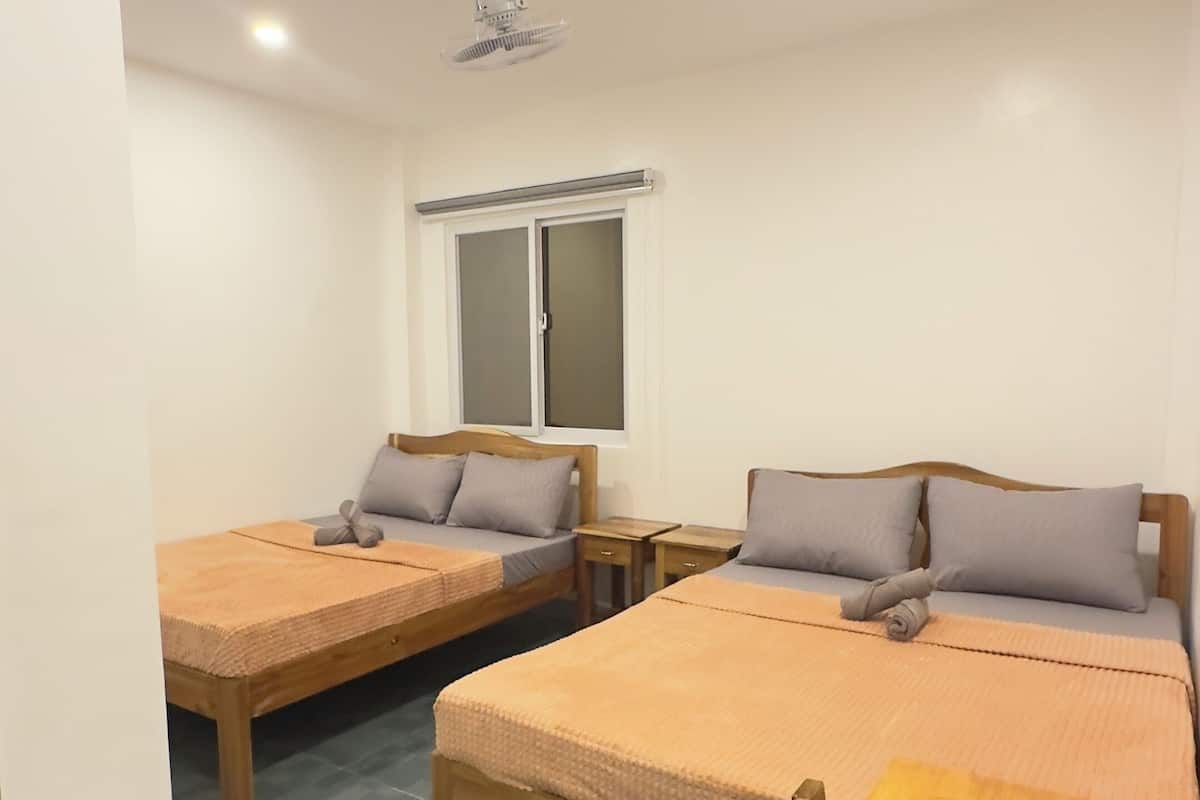 A room with two beds, a wooden table, and a window with frosted glass.