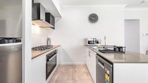 Una cocina moderna con electrodomésticos de acero inoxidable, horno empotrado, lavavajillas y un reloj en la pared.