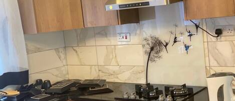 A kitchen with wooden cabinets, a stainless steel range hood, a marble backsplash, and a coffee maker on the counter.
