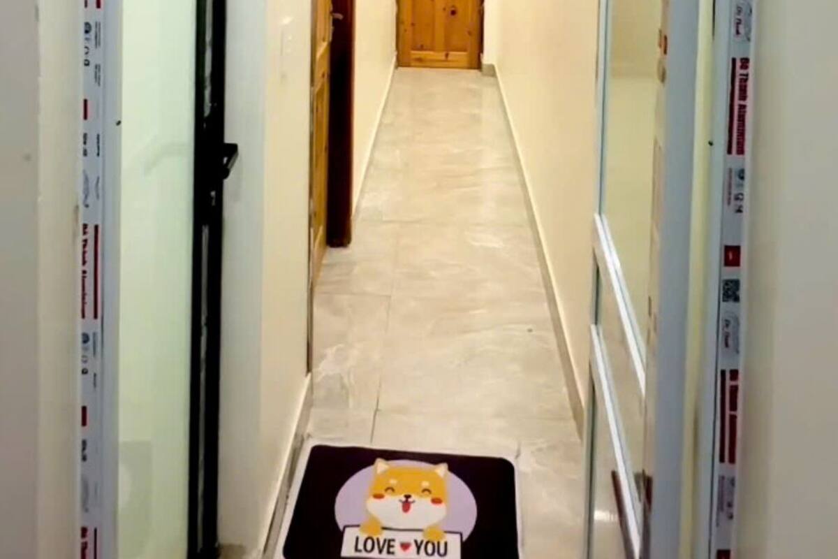 A hallway with a wooden door at the end, a mat with a dog illustration, and a sign with the number 202.