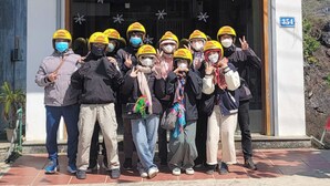 Un groupe de personnes se tient devant l’hôtel TOTO CHAN, portant des casques et faisant le signe de la paix.