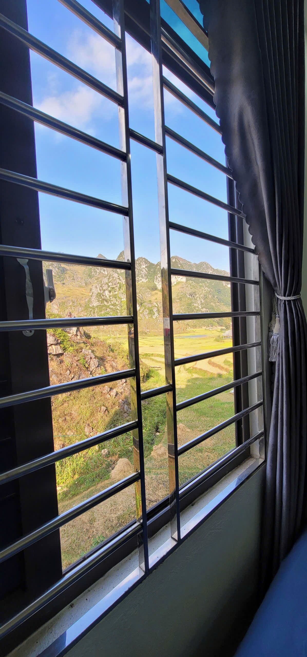 Una ventana con barrotes, vista de un paisaje montañoso y una cortina.