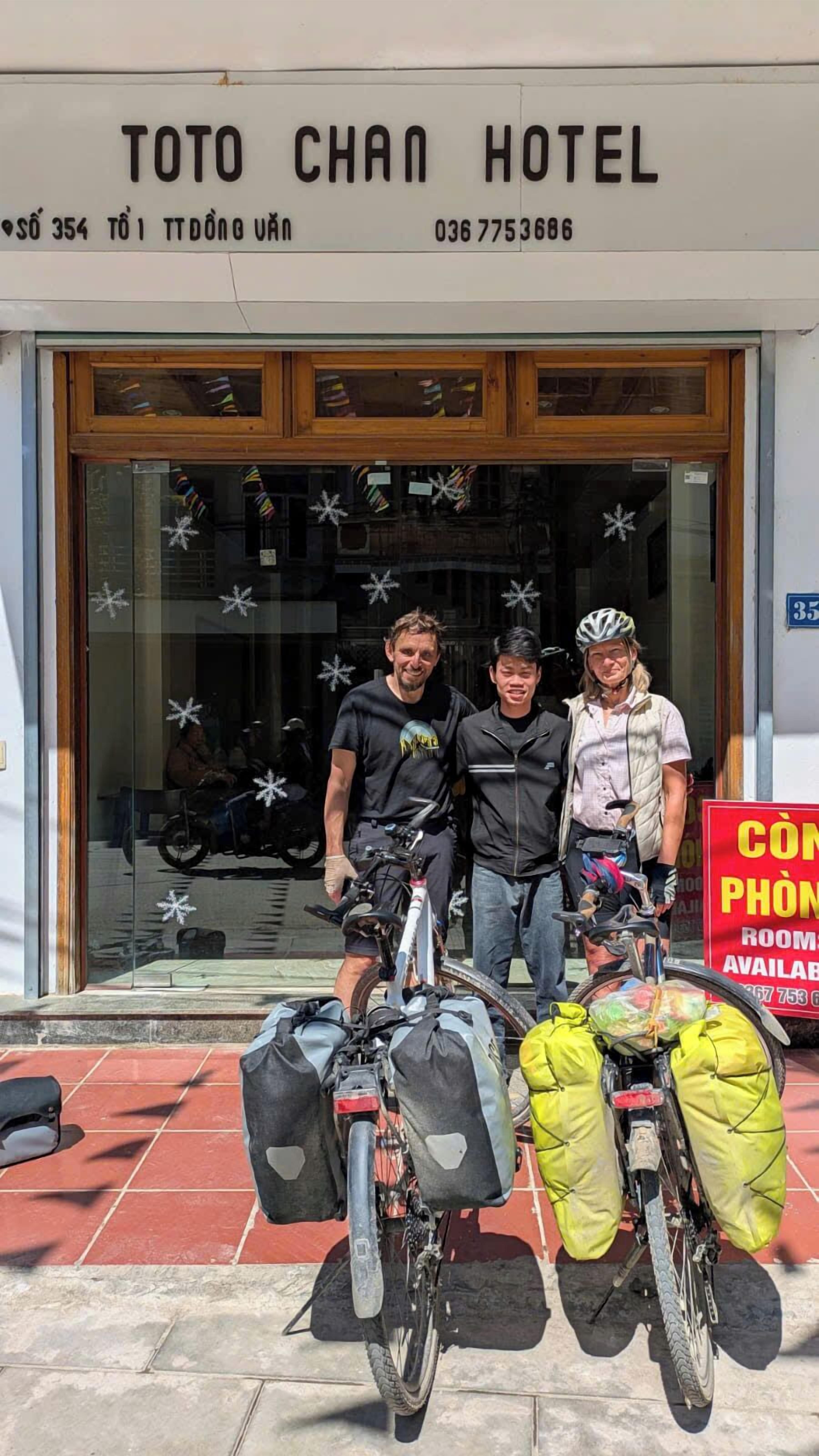 A hotel entrance with three bicycles parked in front, a signboard with contact information, and a window decorated with snowflakes.