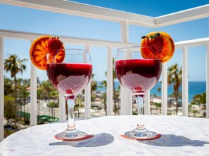 Two glasses of red beverage with fruit garnishes on a table with a white tablecloth, overlooking a coastal view. - 309 Acapulco Playa de Las Americas (Playa de las Américas)