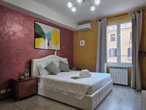 A bedroom with a bed, a nightstand, a painting, an air conditioning unit, and a window with curtains. - Giovanni Giolitti 177 Termini (Rome)