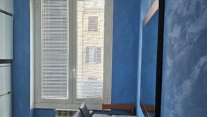 A room with a blue wall, a window with blinds, a table with chairs, and a radiator. - Giovanni Giolitti 177 Termini (Rome)