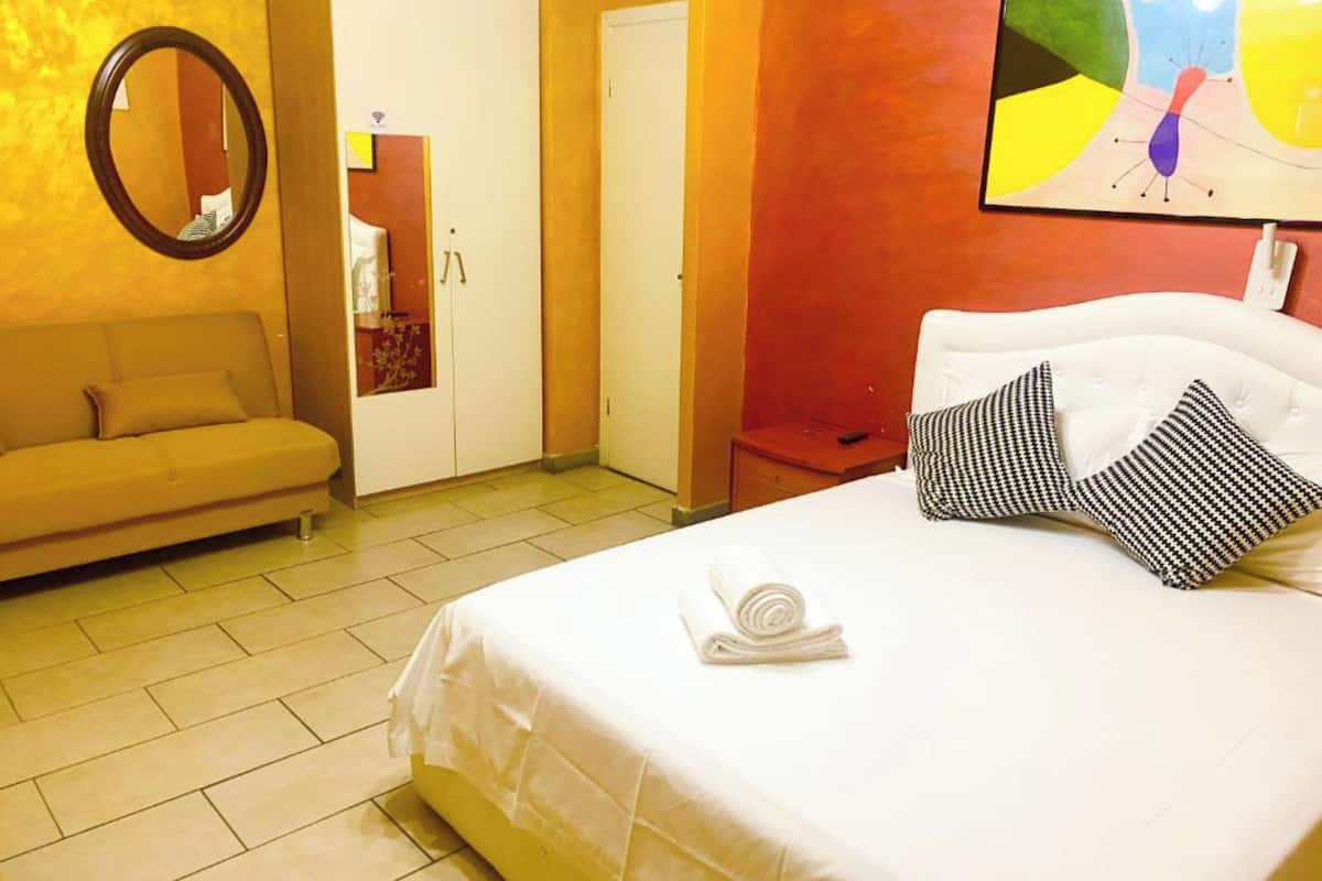 Habitación de hotel con cama, sofá, espejo y un cuadro en la pared.