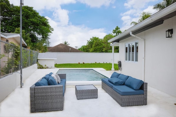 A backyard with a swimming pool, two grey wicker sofas with blue cushions, and a small table. - Coral Cove: Nearby Baha Mar, Pool & Patio, Gated, Beach Walkable (Nassau)