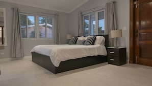 A bedroom with a bed, nightstands, a wooden door, and windows with curtains.
