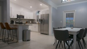 A modern kitchen with white cabinets, a stainless steel refrigerator, and a dining area with a table and chairs.
