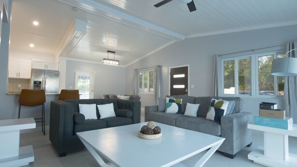 A modern living room with a grey sofa set, a white coffee table, and a kitchen area in the background.