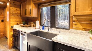 Une cuisine moderne avec des meubles en bois, un évier en acier inoxydable et une fenêtre donnant sur les arbres.