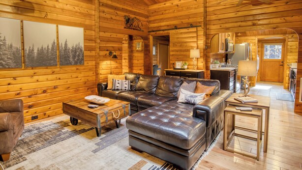 L’intérieur d’une cabane en rondins, avec un canapé en cuir, une table basse en bois et un coin repas.