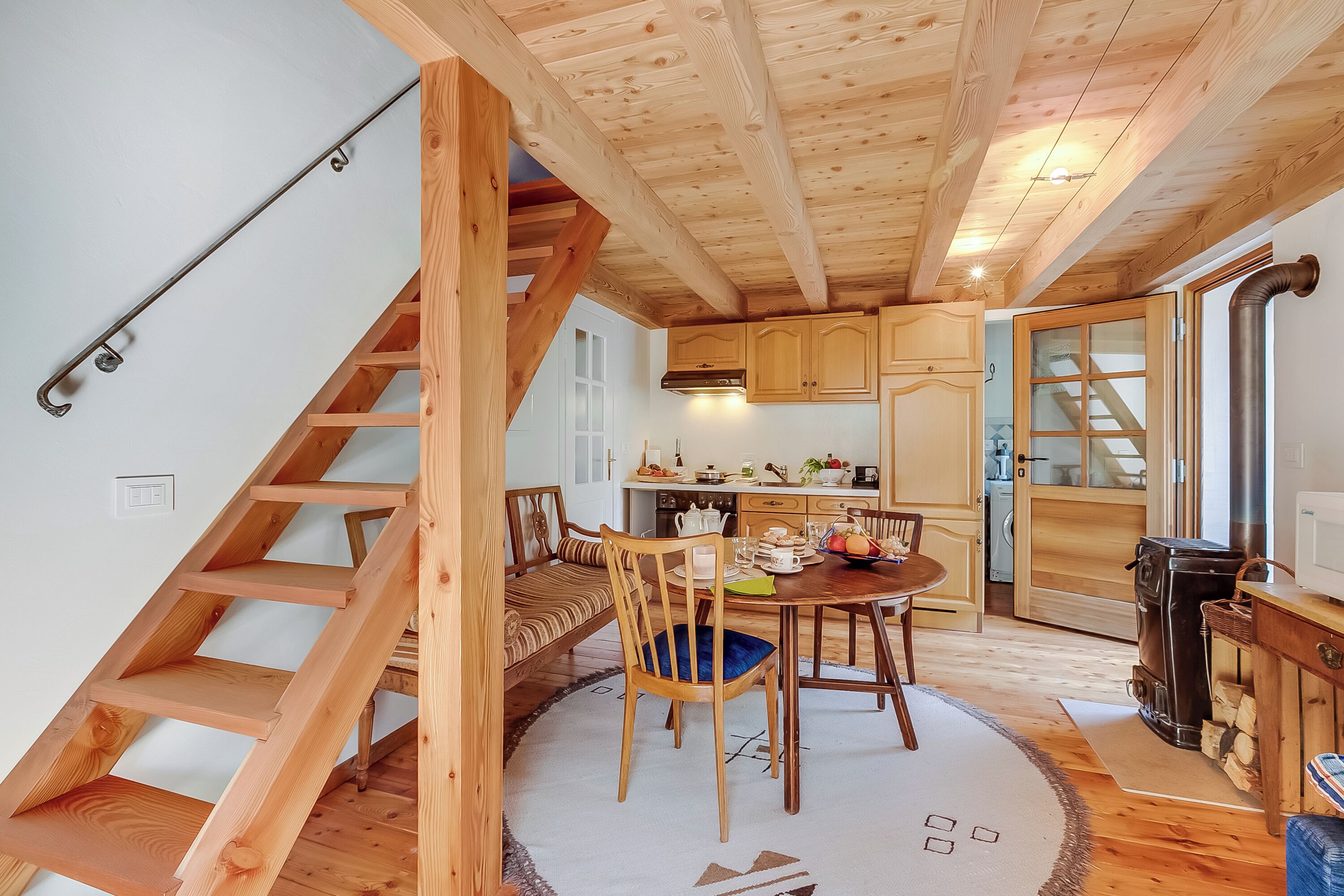 Ein Holzinnenraum mit Treppe, einem Essbereich mit rundem Tisch und Stühlen sowie einer Küche mit Holzschränken und Herd.
