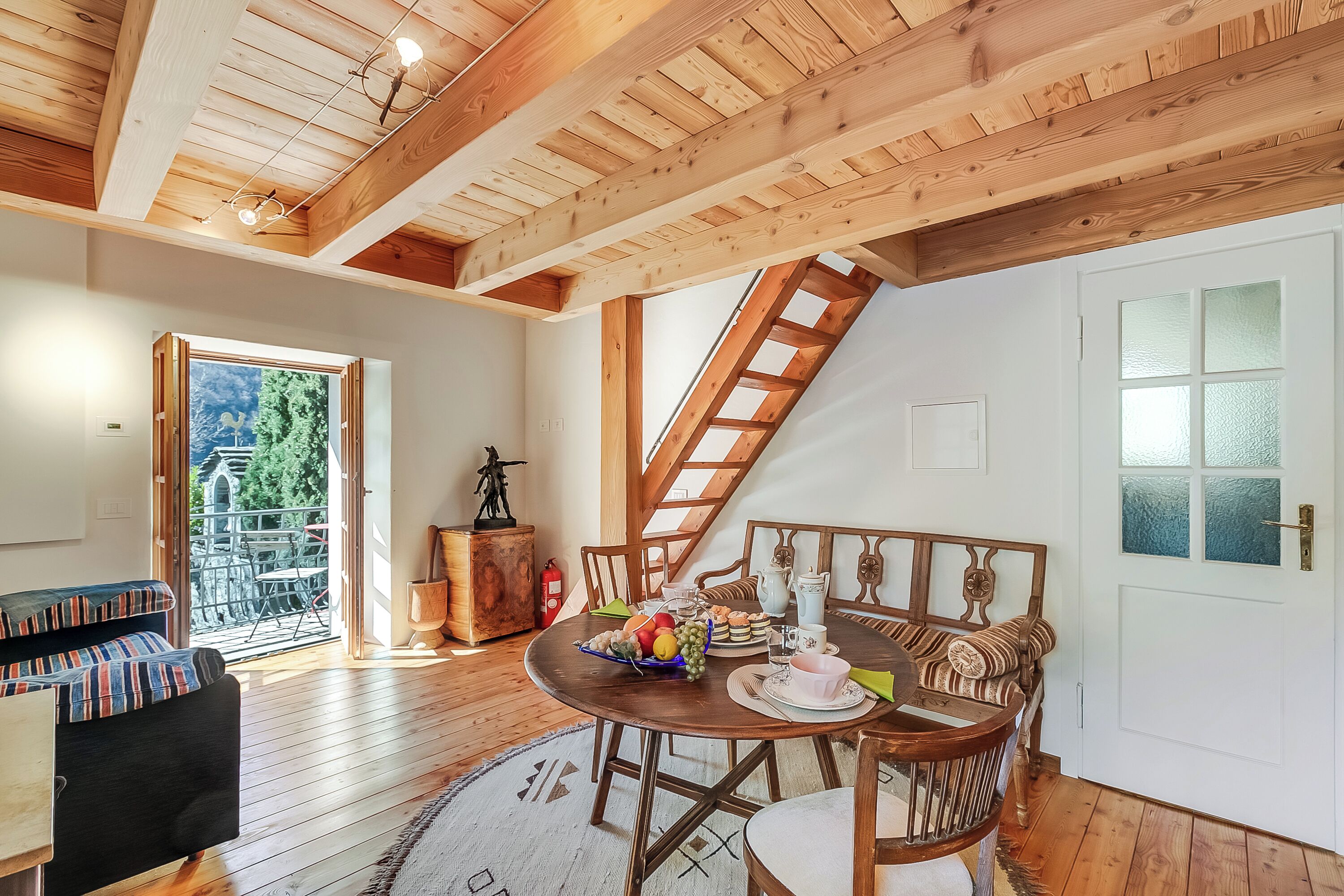 Ein gemütlicher Raum mit Holzboden, einem Tisch gedeckt mit Speisen, einer Couch und einer Treppe, die in einen oberen Bereich führt.