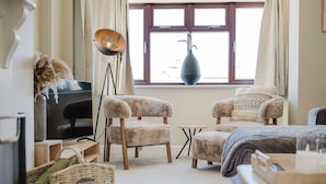 Een gezellige woonkamer met twee comfortabele fauteuils, een klein rond tafeltje, een televisie en een groot raam met gordijnen.