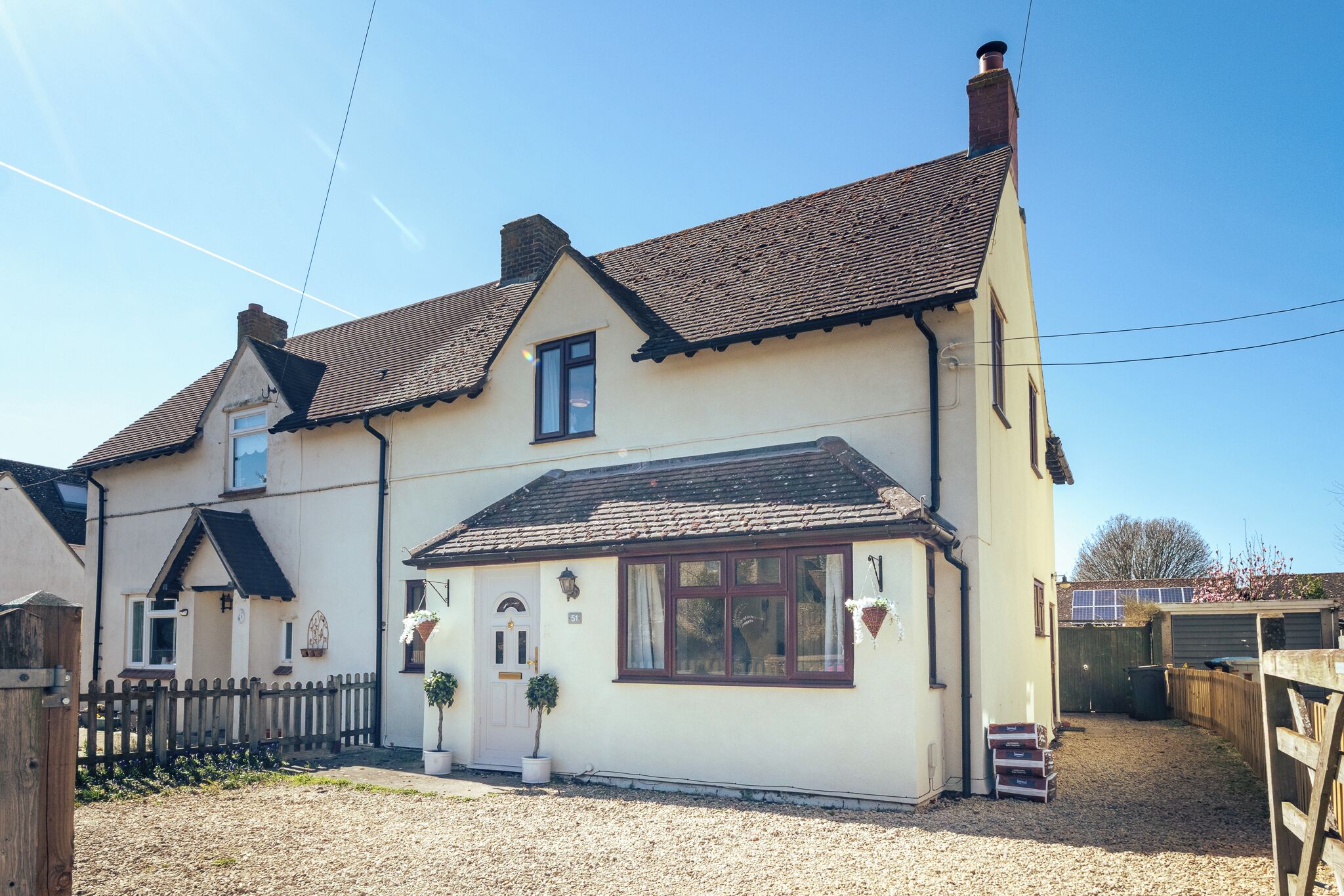 Une maison à deux étages, avec un toit en tuiles, un porche à l’avant et une cour clôturée.