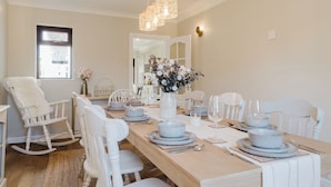 Een eethoek met een houten tafel voor vier personen, witte stoelen en een vaas met bloemen.