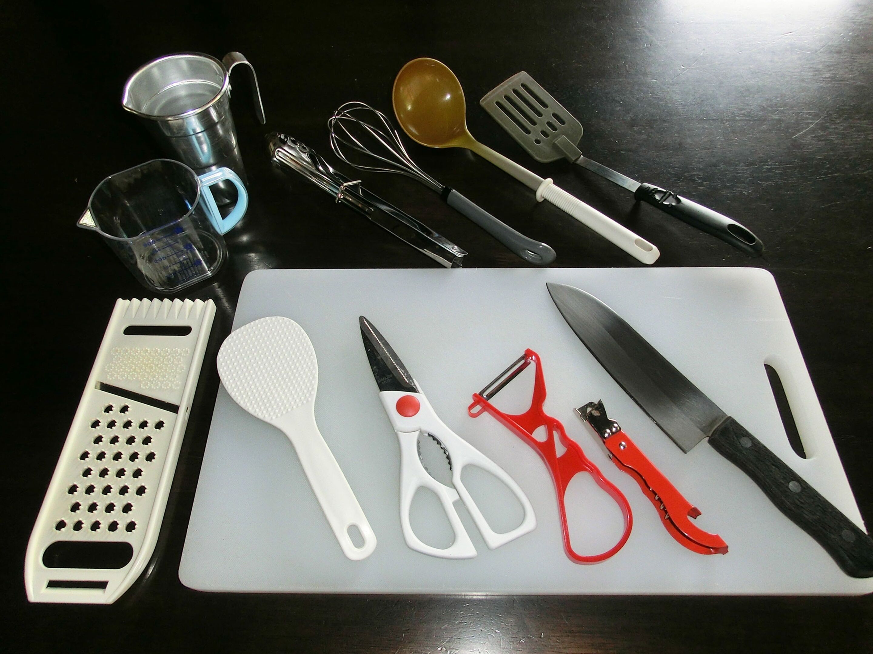 A kitchen counter with various utensils and tools, including a grater, spatula, whisk, and knife.