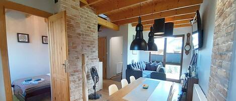 Amplia sala de estar con una gran mesa de comedor de madera, un muro de ladrillo y un rincón de descanso acogedor con cojines.