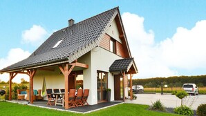 Een tweegevelwoning met een overdekte patio, een eethoek met tuinmeubilair, en een auto op de oprit.