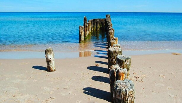 Een zandstrand met een houten constructie die het water in loopt.