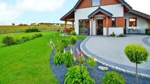 Een modern huis met twee verdiepingen, een overdekte veranda, een aangelegde tuin en een verharde oprit.