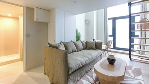 A modern living room with a sofa, a round wooden table, and a large window with a view. - Beautiful AC Duplex Bastille Le Marais (Paris)