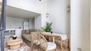 A compact living space with a kitchenette, a dining area with a round table and chairs, and a sofa. - Beautiful AC Duplex Bastille Le Marais (Paris)