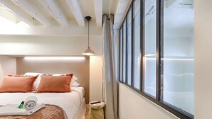 A hotel room with a bed, a small round table, a window, and a hanging light fixture. - Beautiful AC Duplex Bastille Le Marais (Paris)