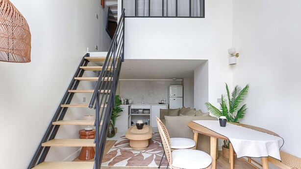 A modern interior with a staircase leading to a loft area, a dining table with chairs, and a kitchen in the background. - Beautiful AC Duplex Bastille Le Marais (Paris)