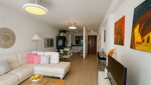 A modern living room with a white sofa, a dining table, and a kitchen in the background. - Varanda do Sol – Private Terrace with Sea View in Funchal (Funchal)