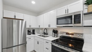 A modern kitchen with white cabinets, a stainless steel refrigerator, a microwave, a stovetop, and a coffee maker. - Modern 2BR 3rd Unit (Haltom City)