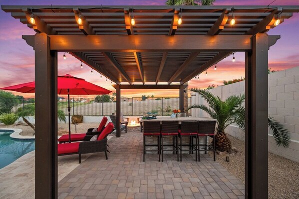 Eine Terrasss mit Pergola, roten Sonnenschirmen und Sitzgelegenheiten.