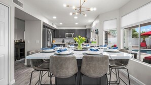A modern kitchen with dark cabinets, stainless steel appliances, and a dining area with a white table and grey chairs. - Par-Fect Views | Red Mountain Golf Course, Heated Pool , Incredible Red Mountain Views (Mesa)