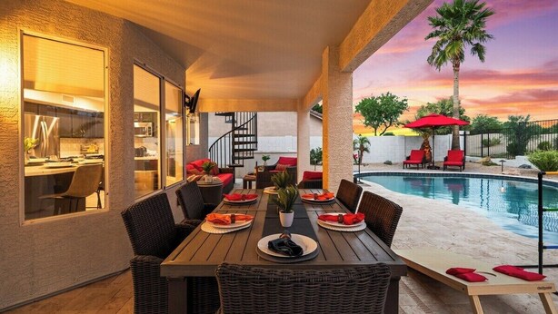 An outdoor dining area with a pool, red chairs, and a view of the sunset. - Par-Fect Views | Red Mountain Golf Course, Heated Pool , Incredible Red Mountain Views (Mesa)