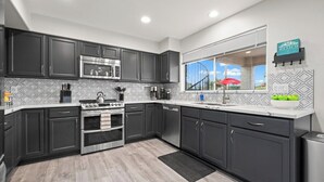 A modern kitchen with dark cabinets, stainless steel appliances, and a large window overlooking a scenic view. - Par-Fect Views | Red Mountain Golf Course, Heated Pool , Incredible Red Mountain Views (Mesa)