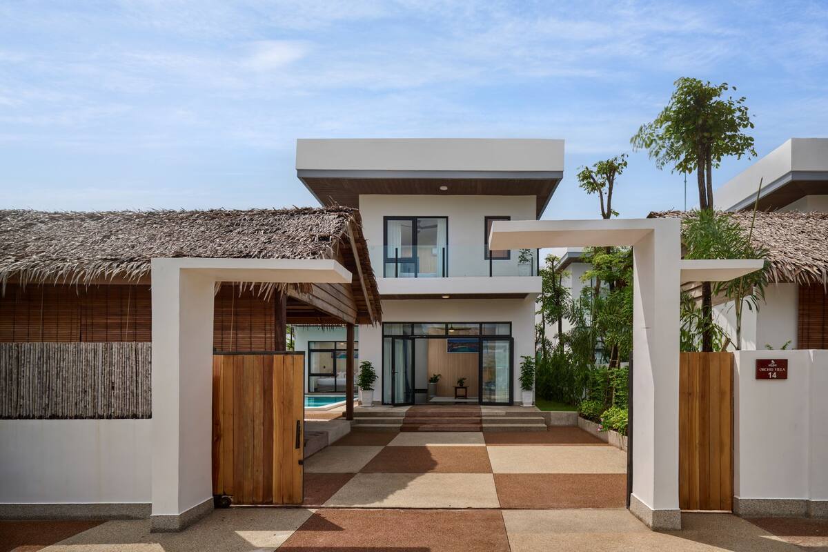 Un hotel moderno con una entrada central, una piscina y una estructura con techo de paja.