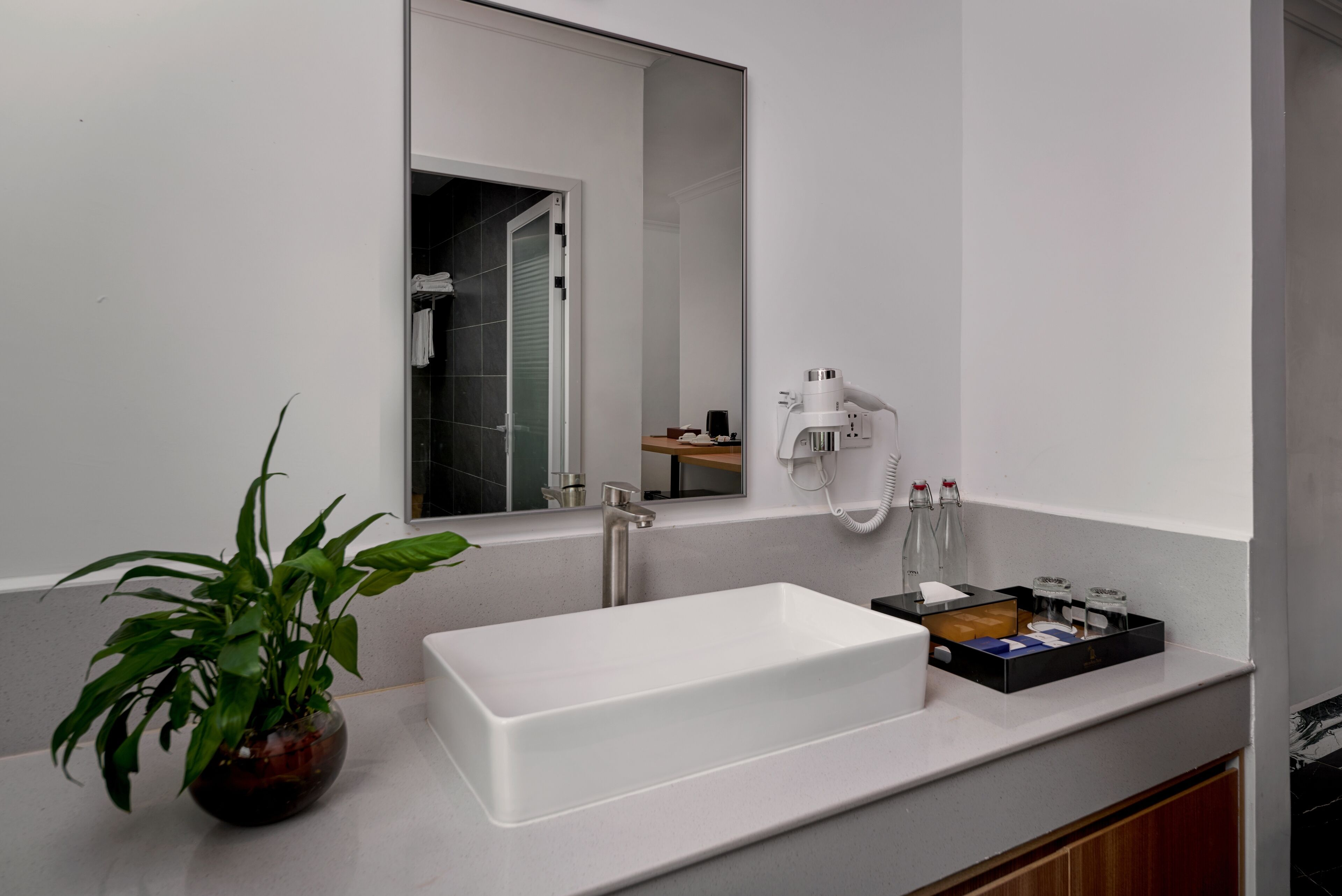 A modern bathroom with a rectangular sink, a large mirror, a potted plant, and a towel rack.